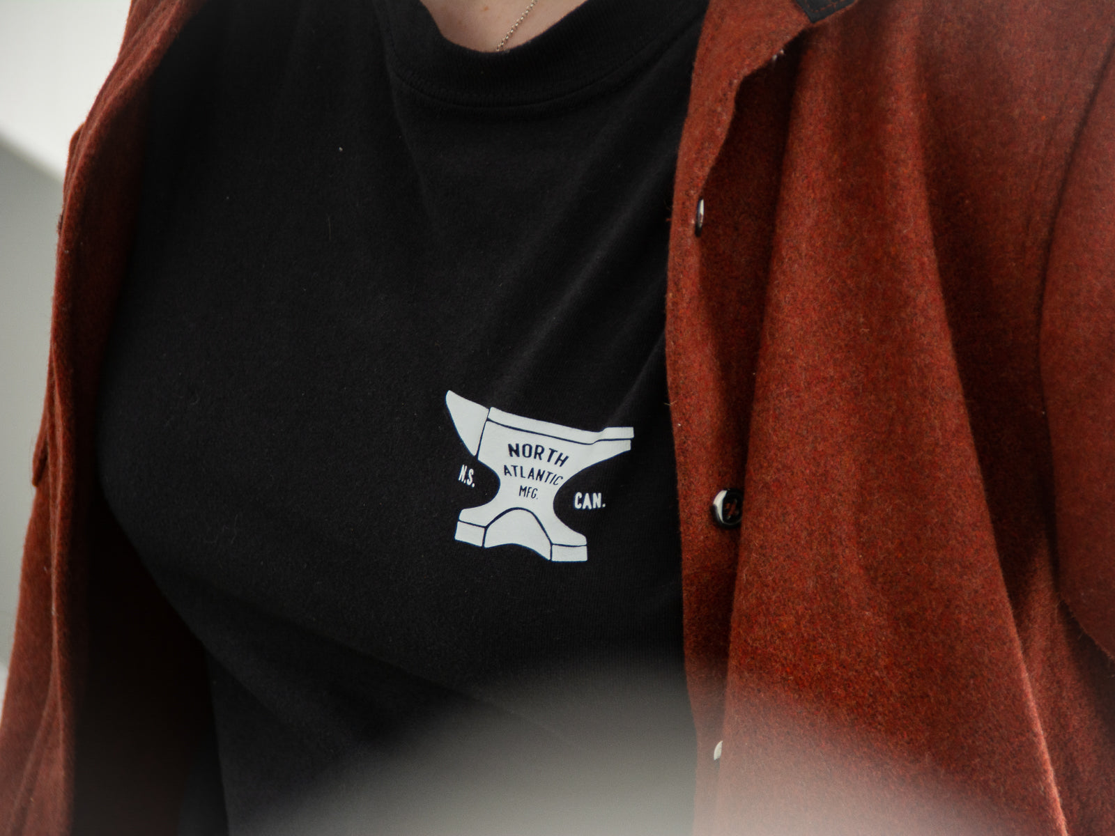 A closeup photo of the front graphic of the black anvil tee with text on the anvil that reads "North Atlantic MFG - N.S. CAN.