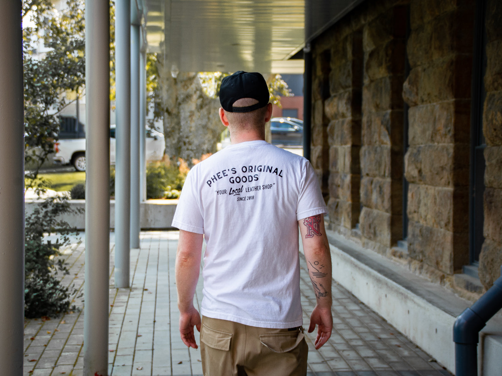 Phee walking down a brick alley showing the back of the Anvil Tee with the "Your local leathershop" text.