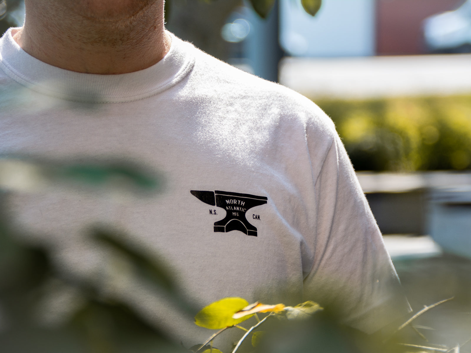 A closeup photo of the front graphic of the white anvil tee with text on the anvil that reads "North Atlantic MFG - N.S. CAN.