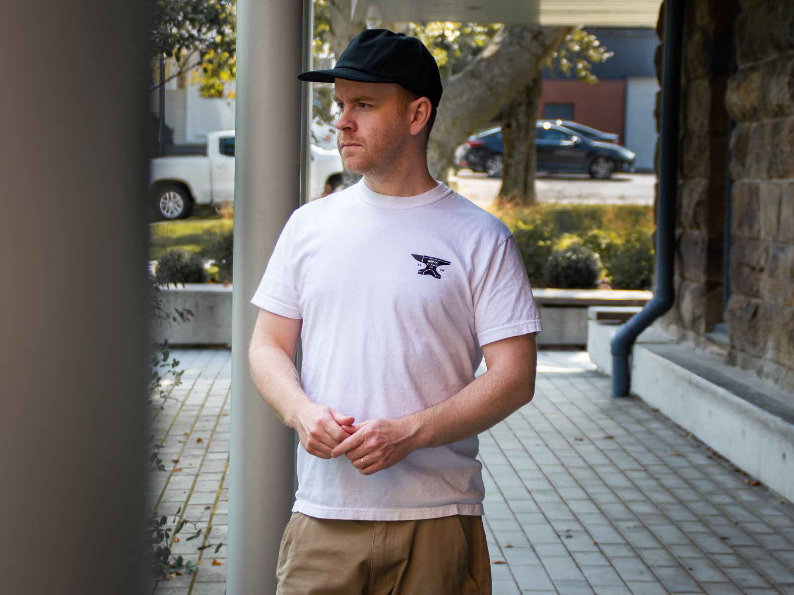 Phee wearing a white Anvil Tee standing under an awning in a brick alley.