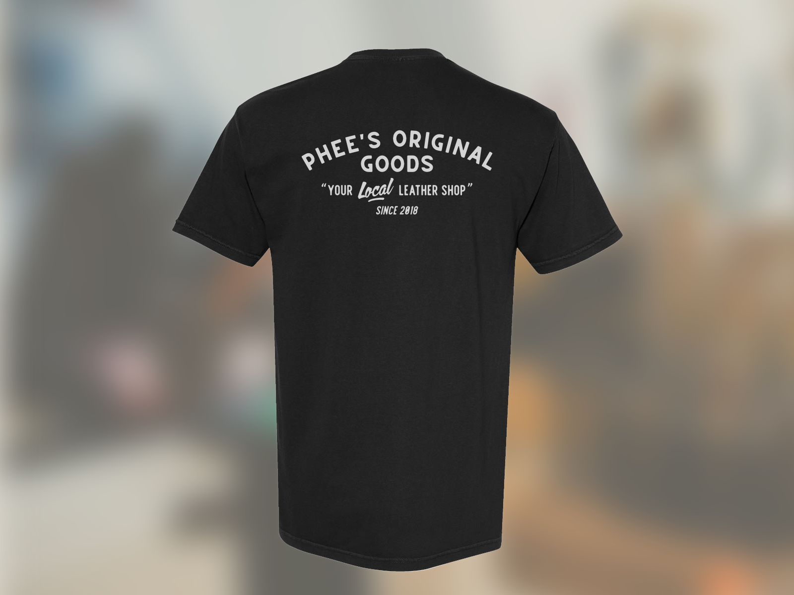 Isolated image of the back of the black anvil tee against a blurred image of the workshop.