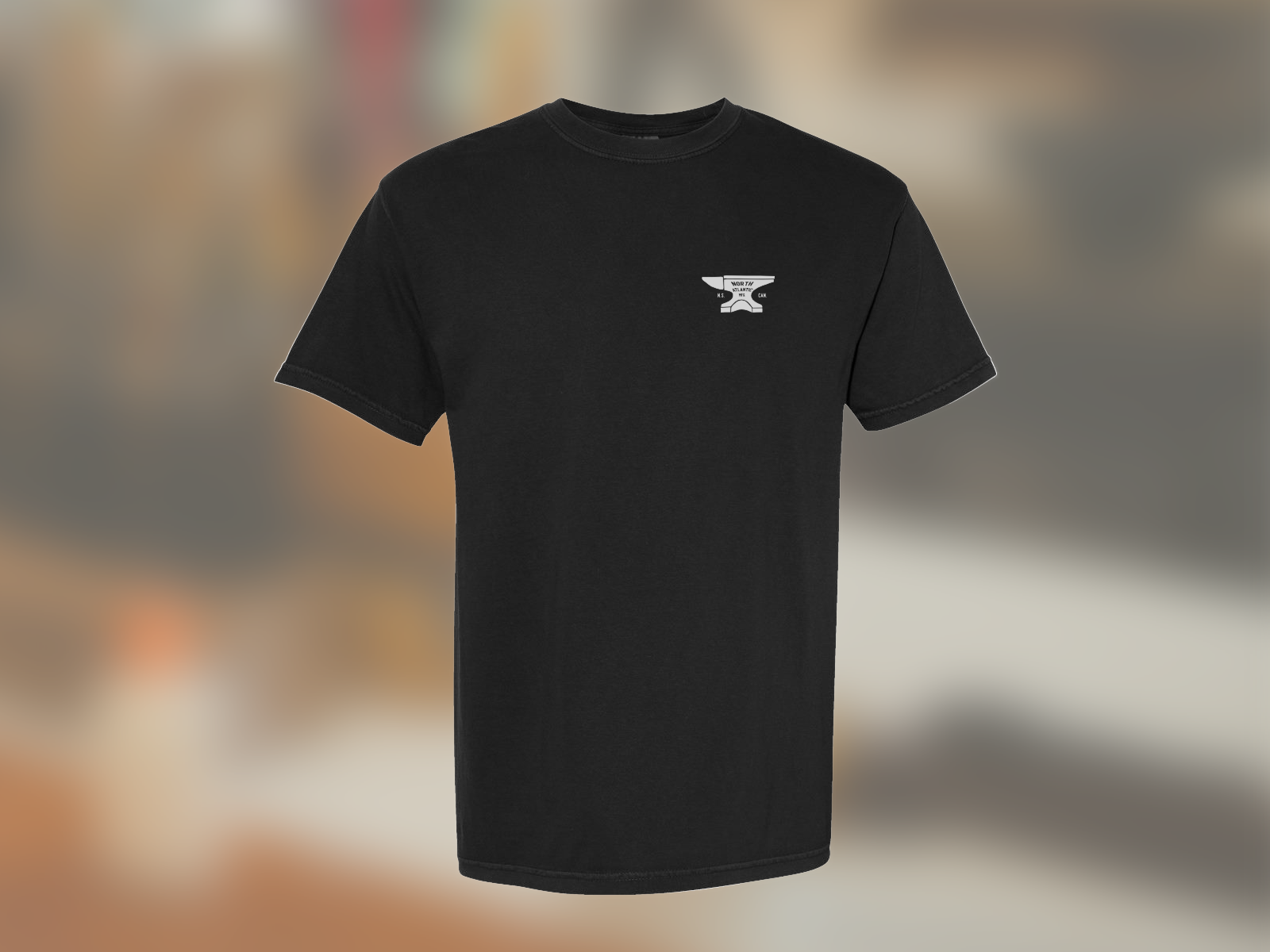 Isolated image of the front of the black anvil tee against a blurred image of the workshop.