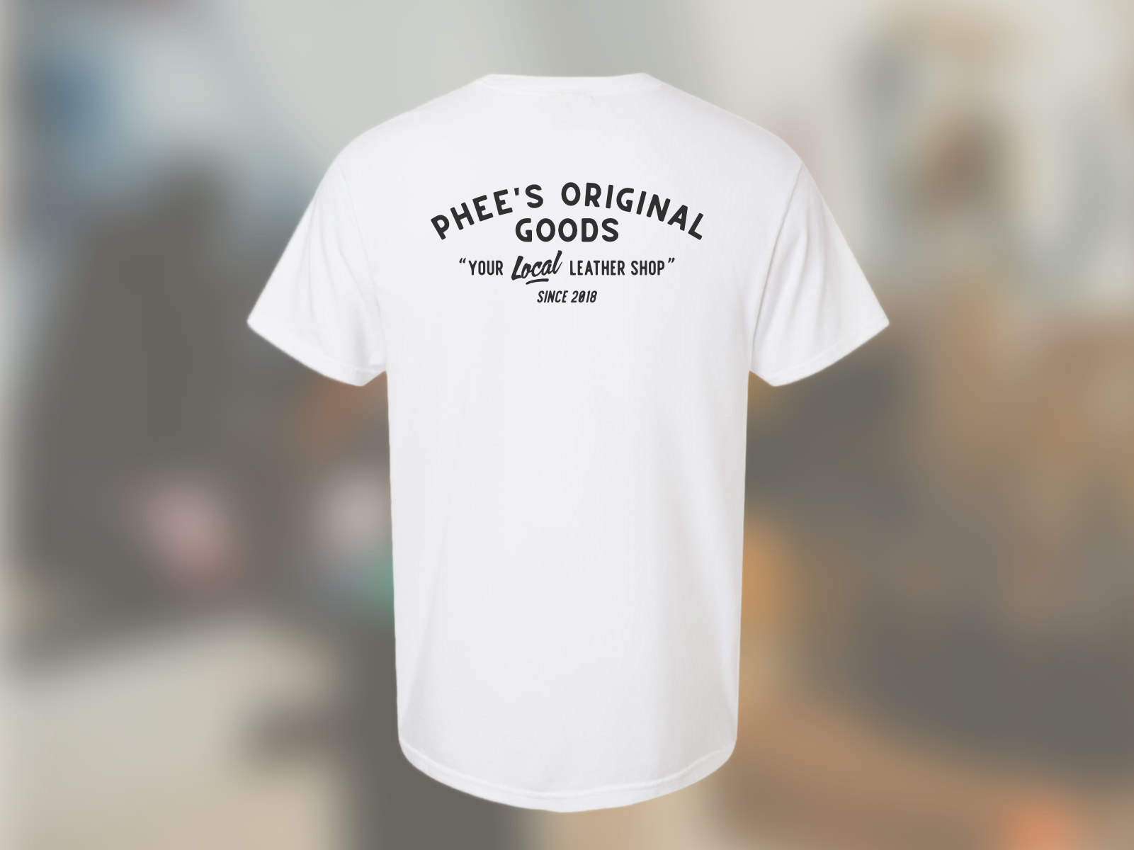 Isolated image of the back of the white anvil tee against a blurred image of the workshop.