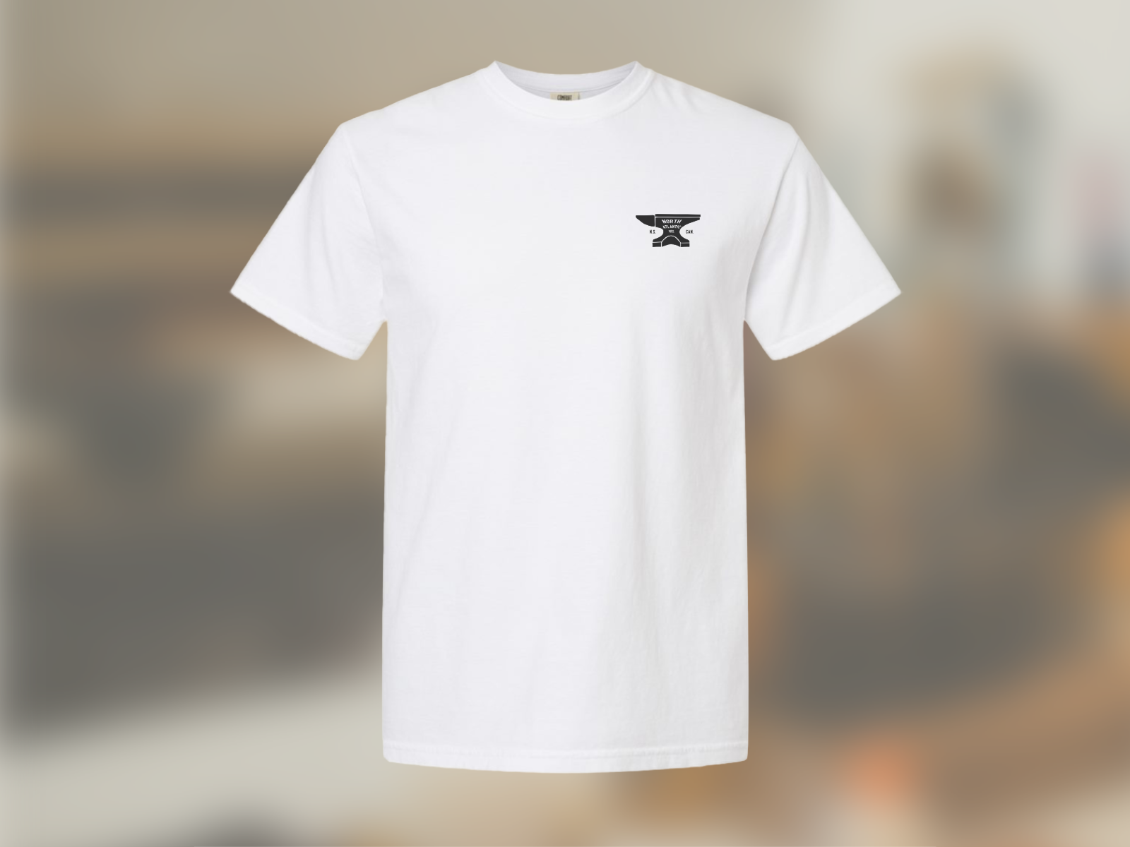 Isolated image of the front of the white anvil tee against a blurred image of the workshop.