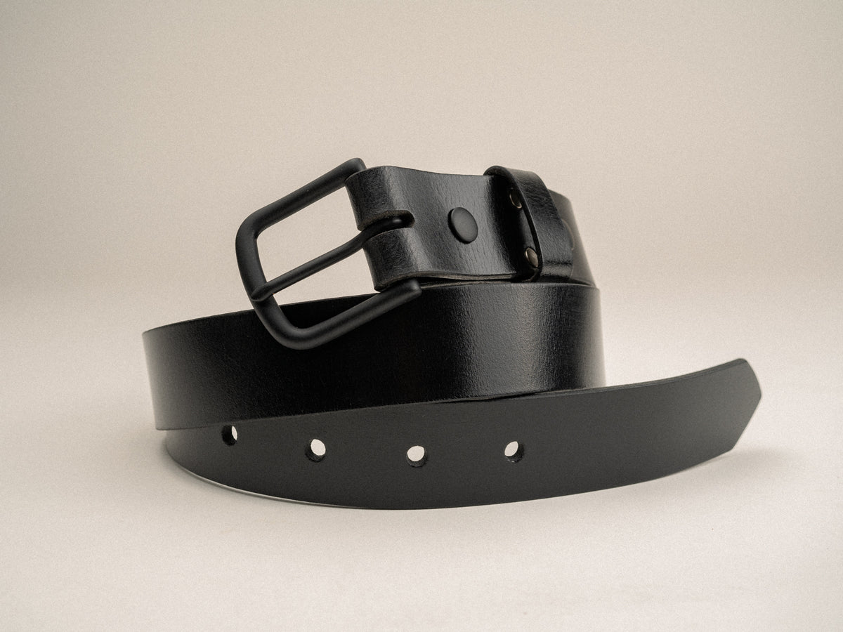 Black leather ashfield belt, with black finished solid brass hardware coiled on a table