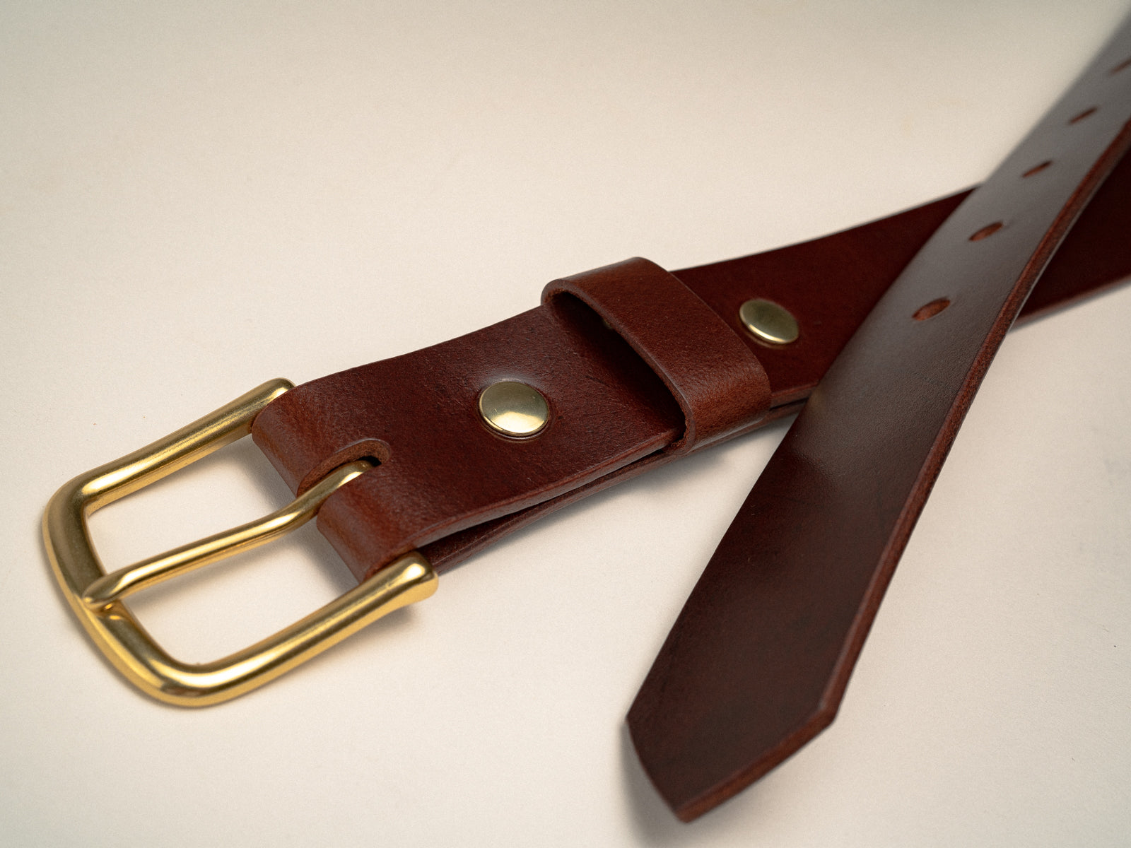 Close up a dark brown ashfield belt with natural brass hardware laying on a table