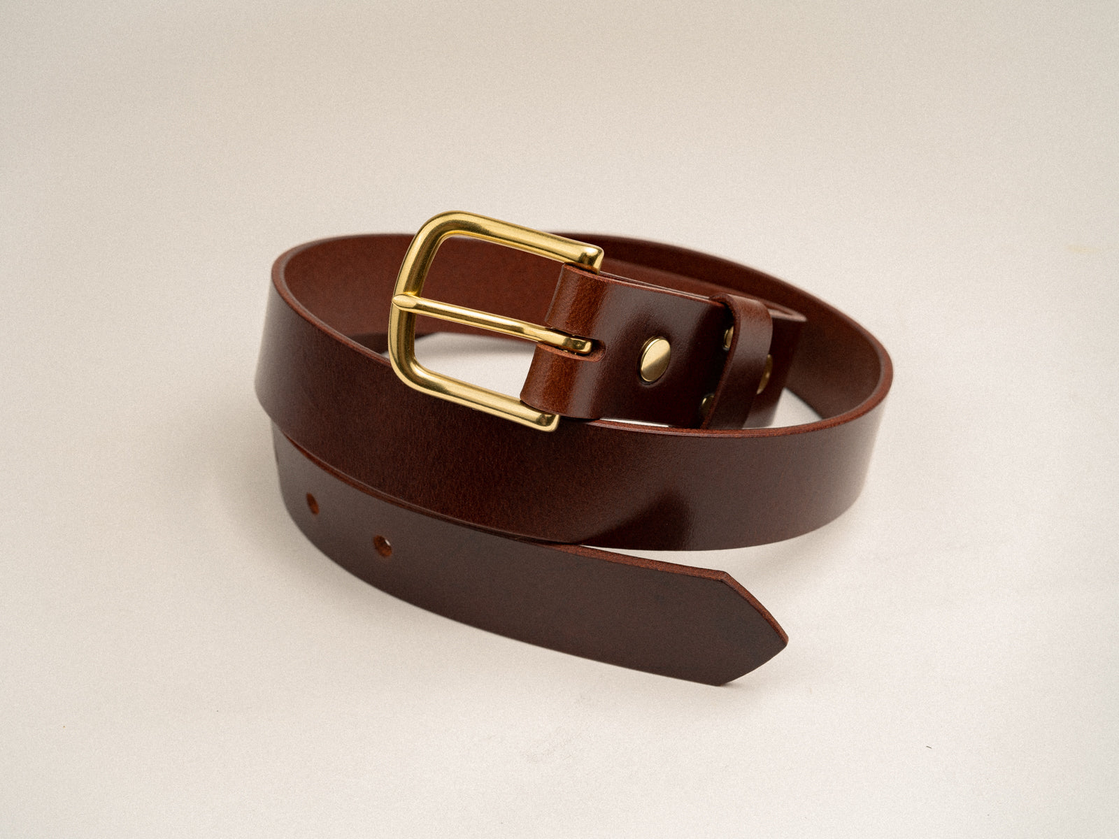 Handmade brown leather Ashfield belt with natural brass hardware coiled on a table