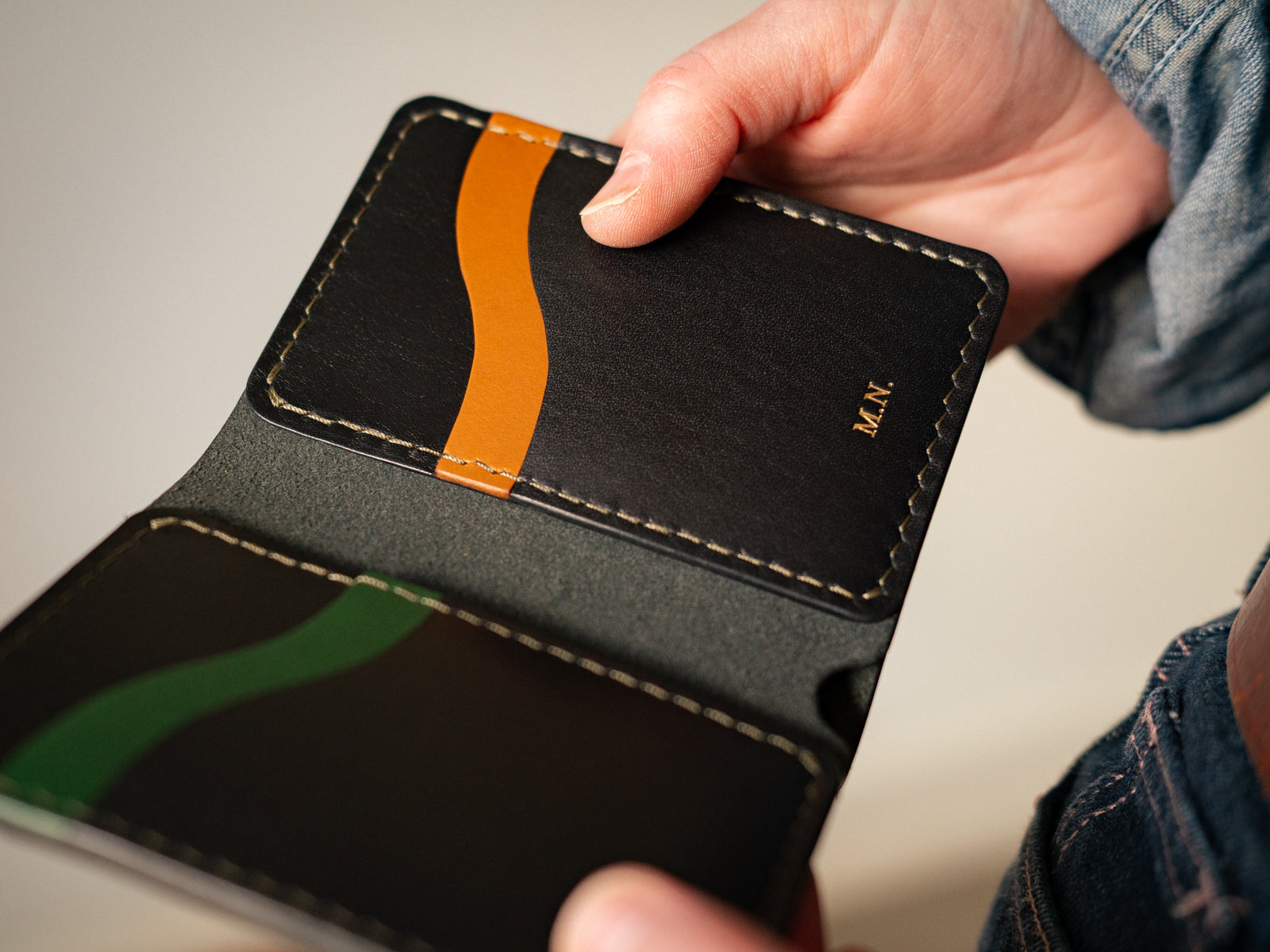 Custom made Bateston wallet in black, tan and pine leather, held in hands
