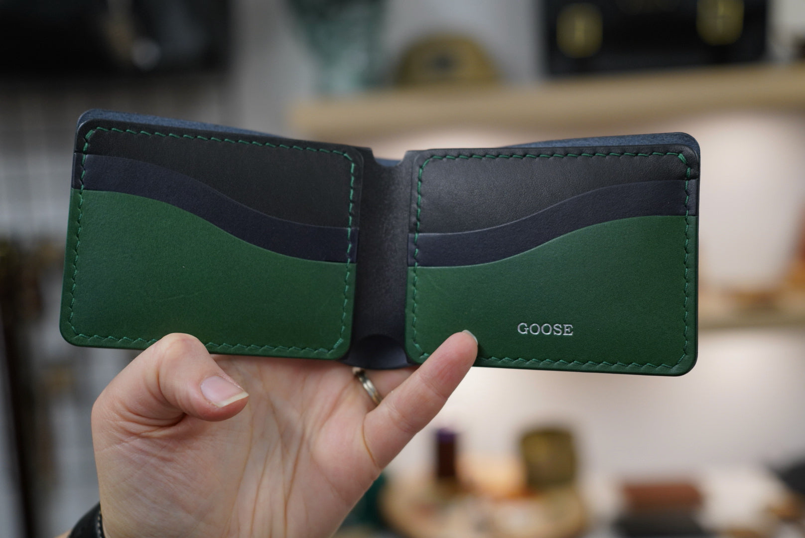 Hand holding a custom made build your own bucklaw bifold wallet with black, navy and pine leather, hand sewn with pine thread. custom silver foil personalization