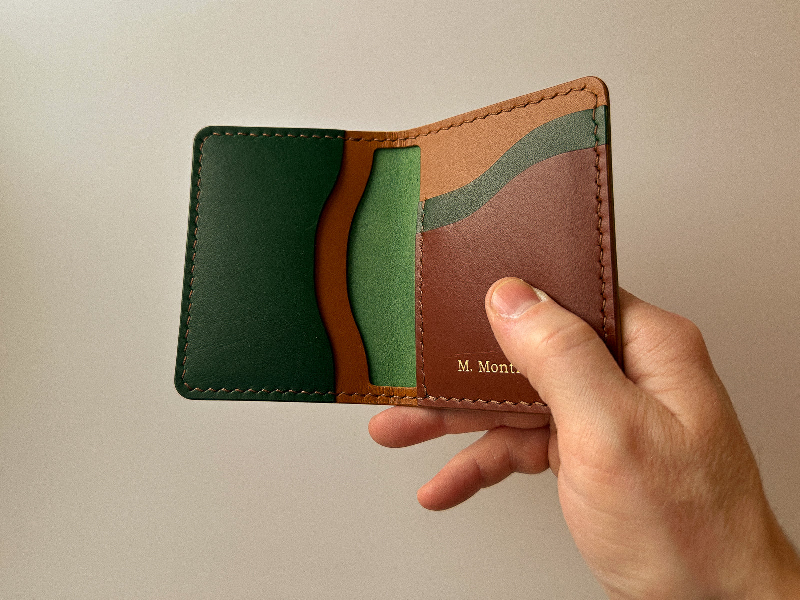 Hand holding a handmade build your own custom Barra leather wallet in pine green, tan and brown