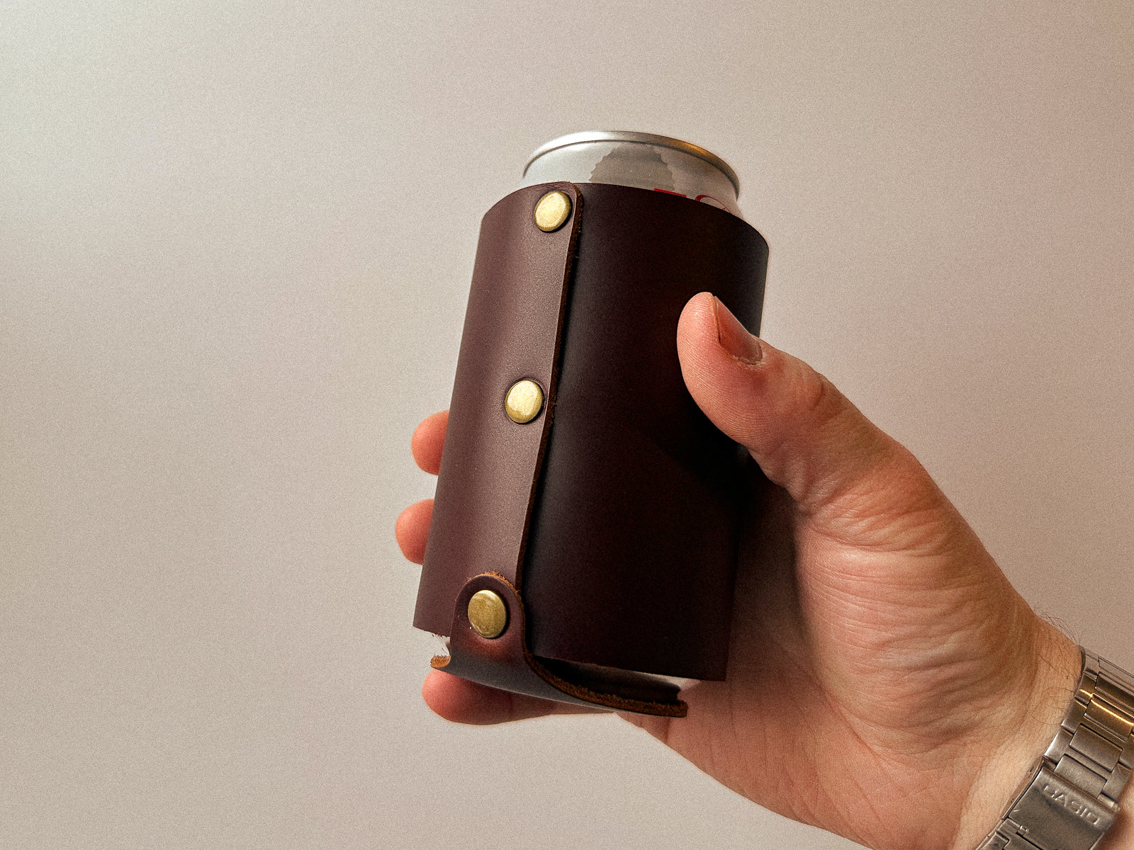hand holding a brown can coozie with riveted seam