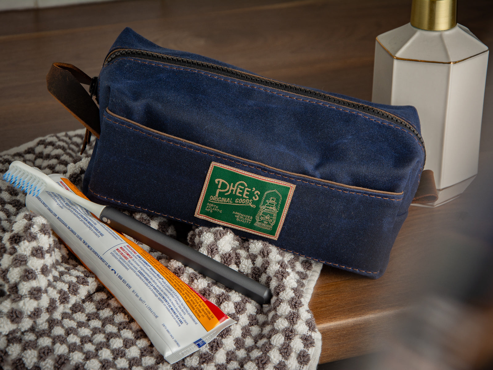 Navy blue waxed canvas Washabuck shaving kit sitting on a bathroom vanity with toiletries