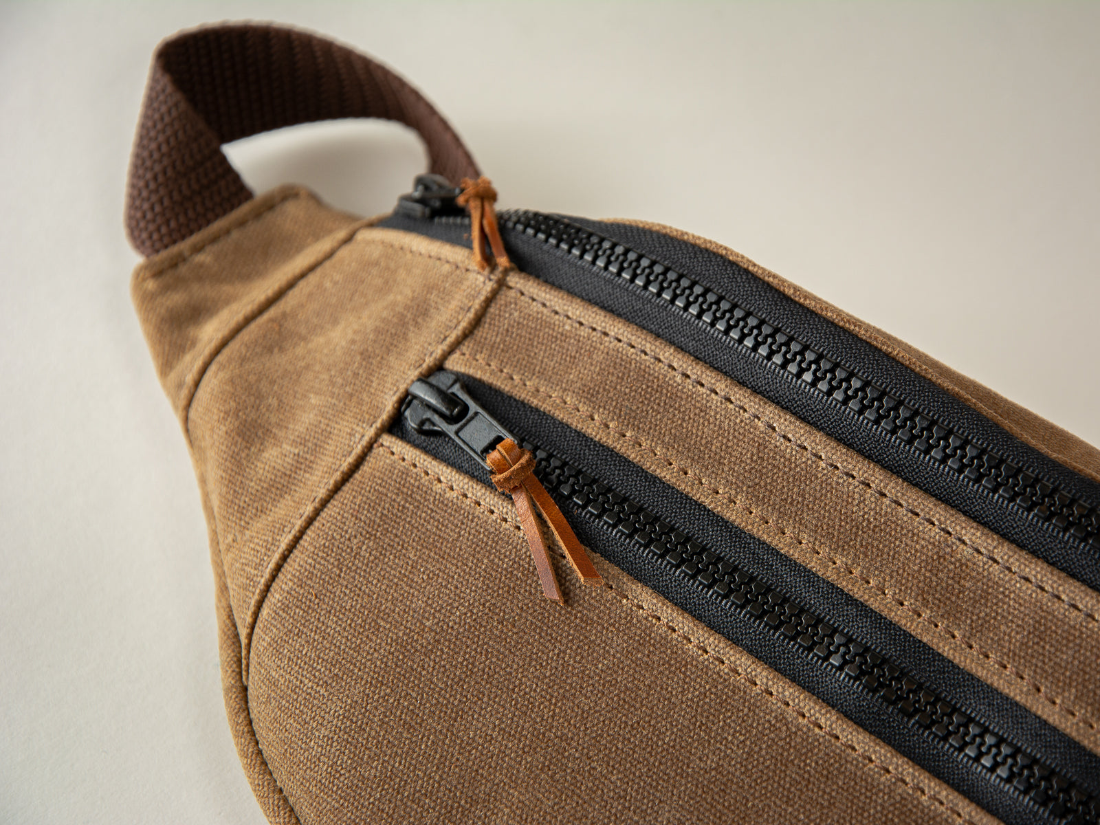 brown sling fanny pack brown leather accents and black zip with brown canvas on white background