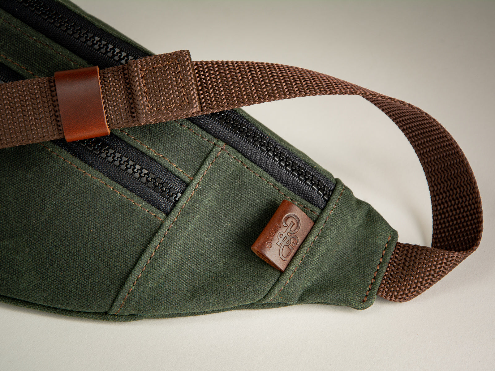 closeup of brown leather tab on green canvas fanny pack with webbing waist or shoulder strap