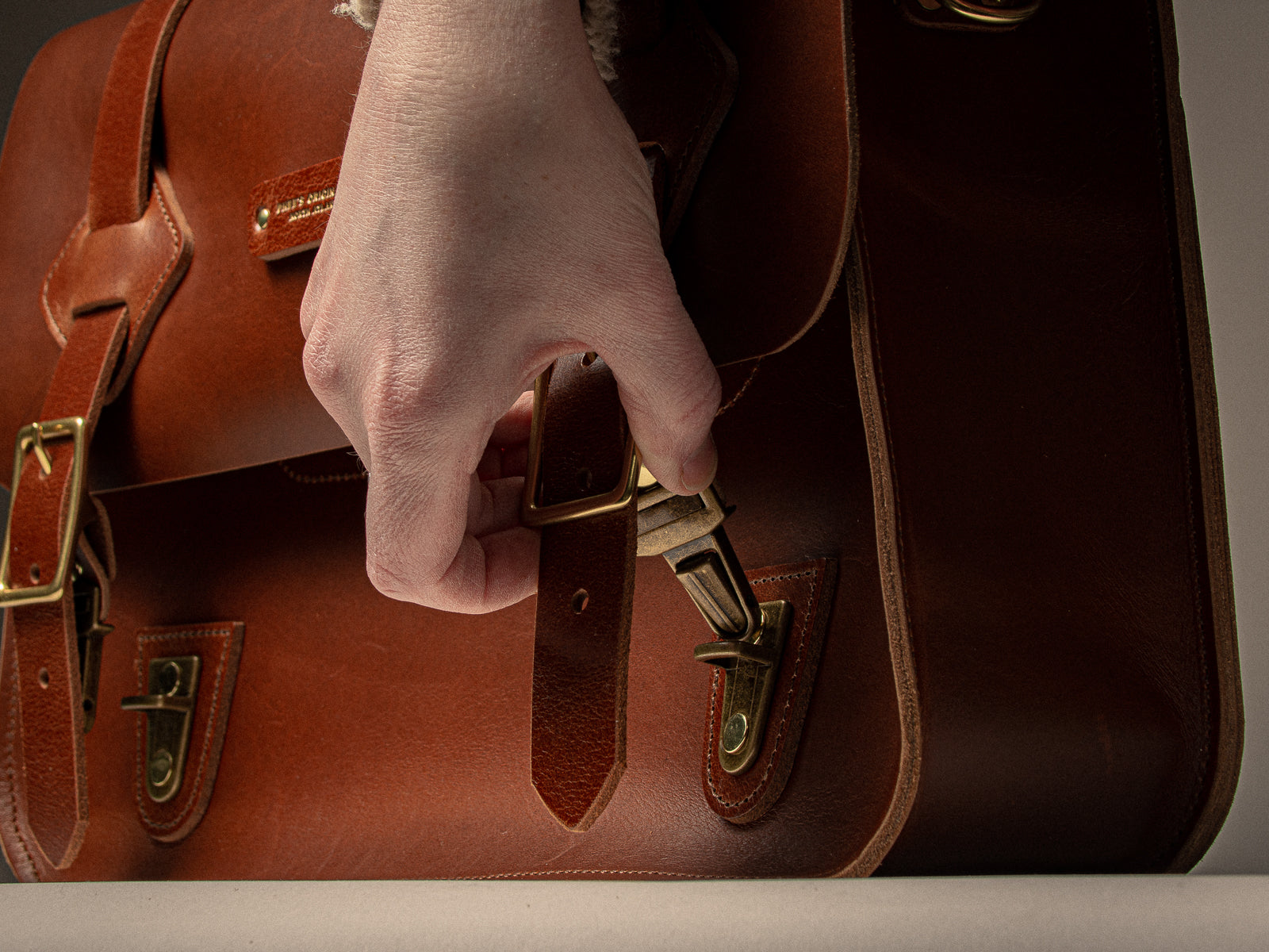 Someone opening a tan leather messenger bag, showing the tuck lock feature