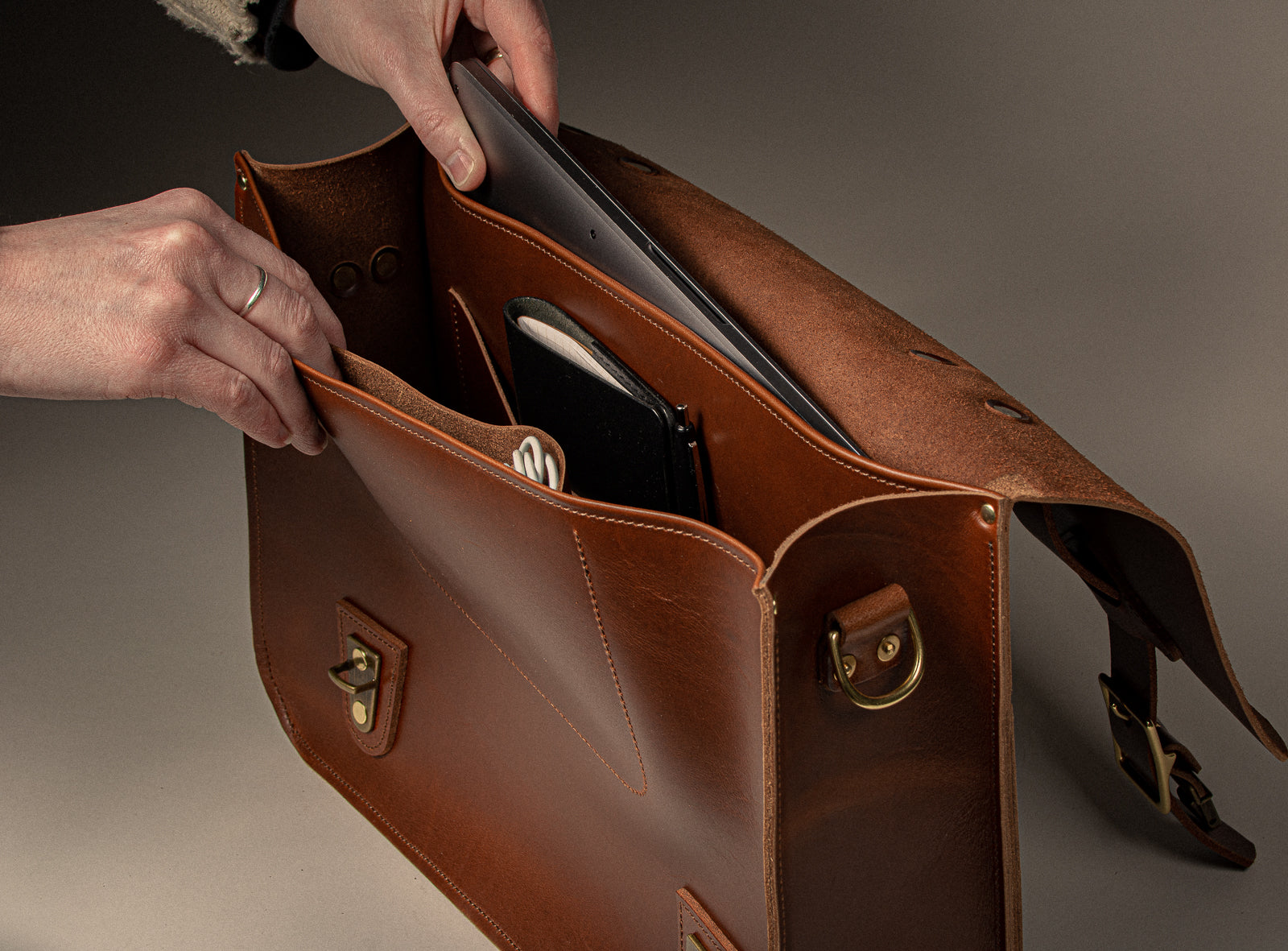 Tan full-grain leather briefcase with person opening it to remove laptop on a beige background