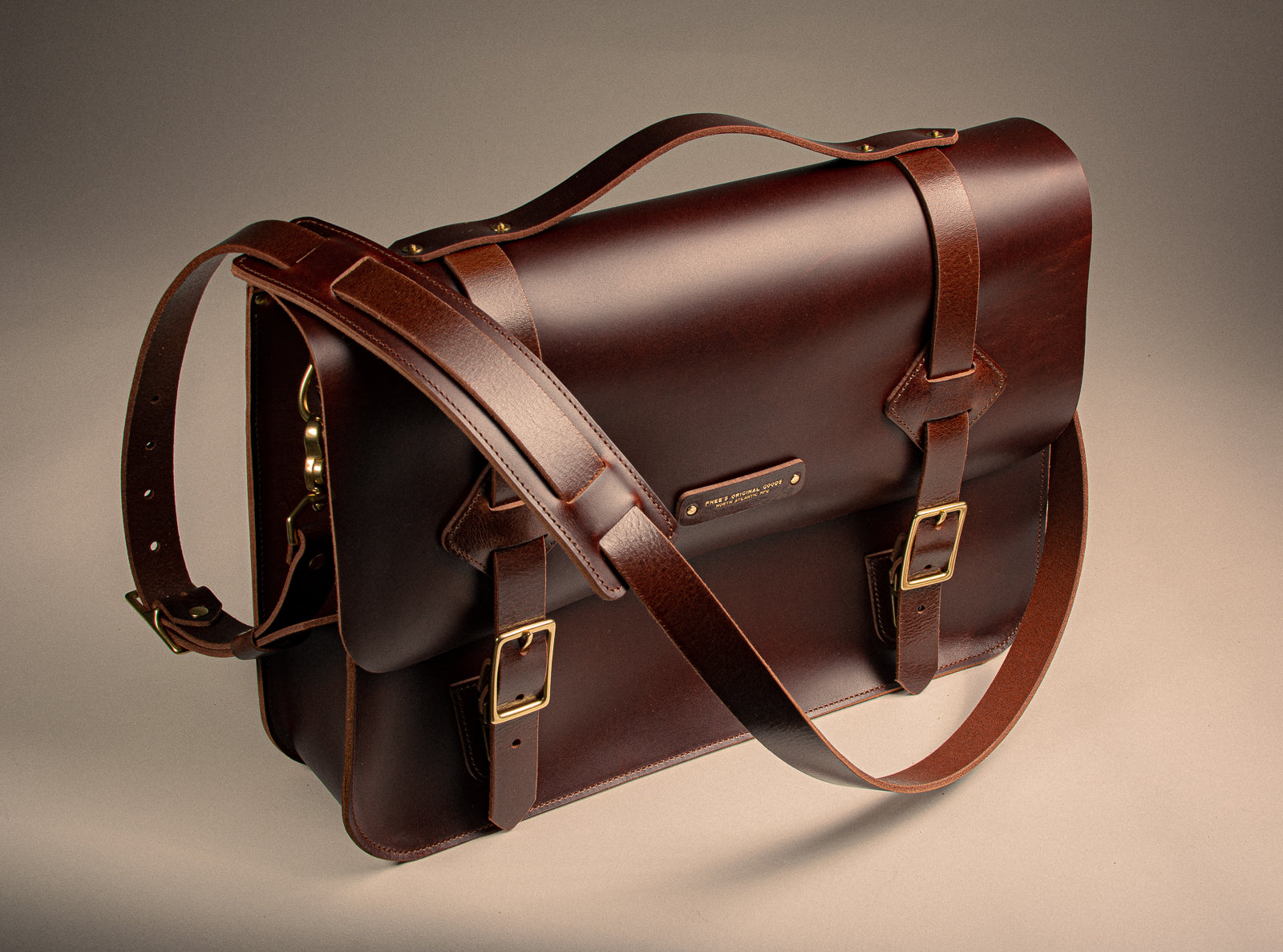 Brown leather side bag with solid brass buckles on a beige background