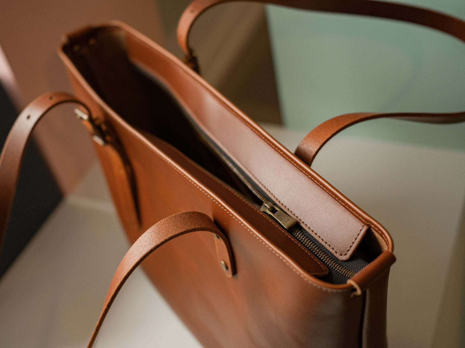 Chestnut Tan Grand Etrang leather handbag with a brass zipper on a light background