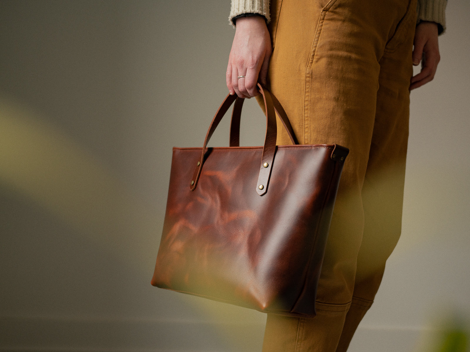 Mahogany brown leather Grand Etant tote bag held by a person