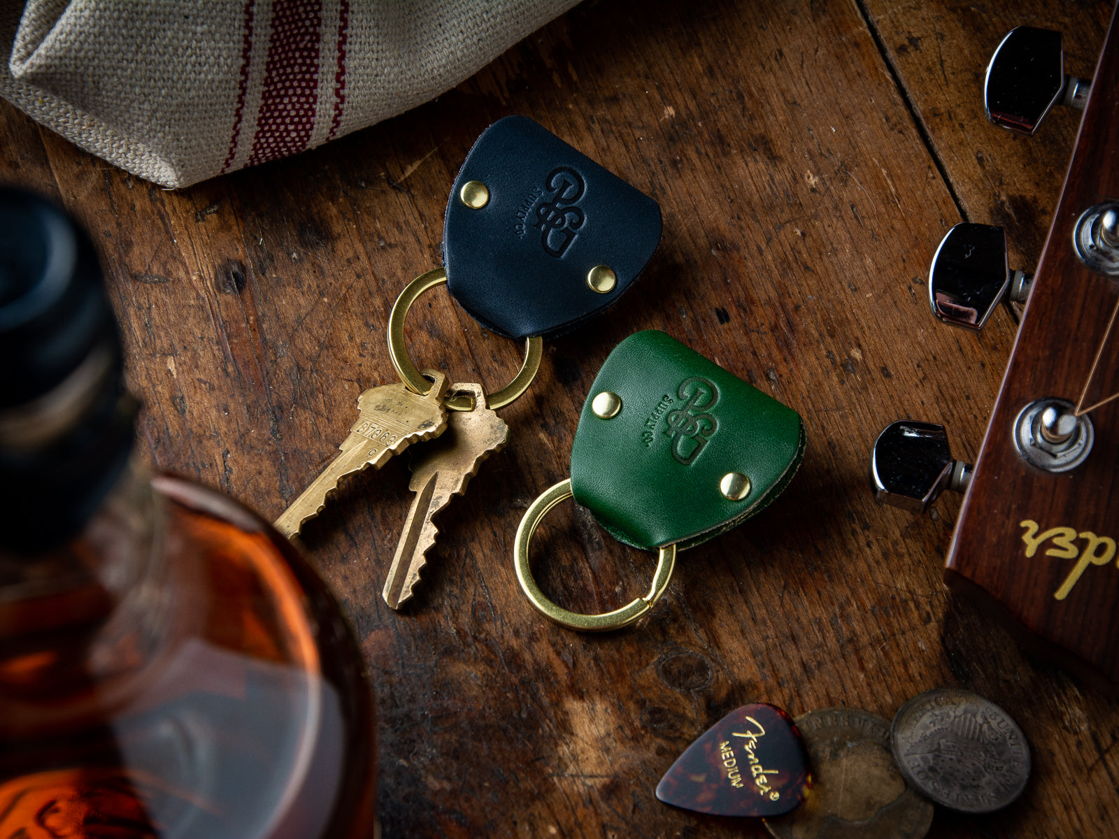 Guitar pick keychains in full grain leather laid out on a table beside an acoustic guitar