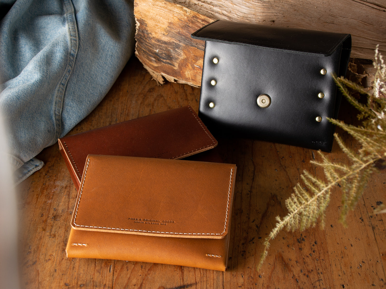 Three fly fishing wallets sitting on wooden table displaying all three available colours, brown, tan, and black.