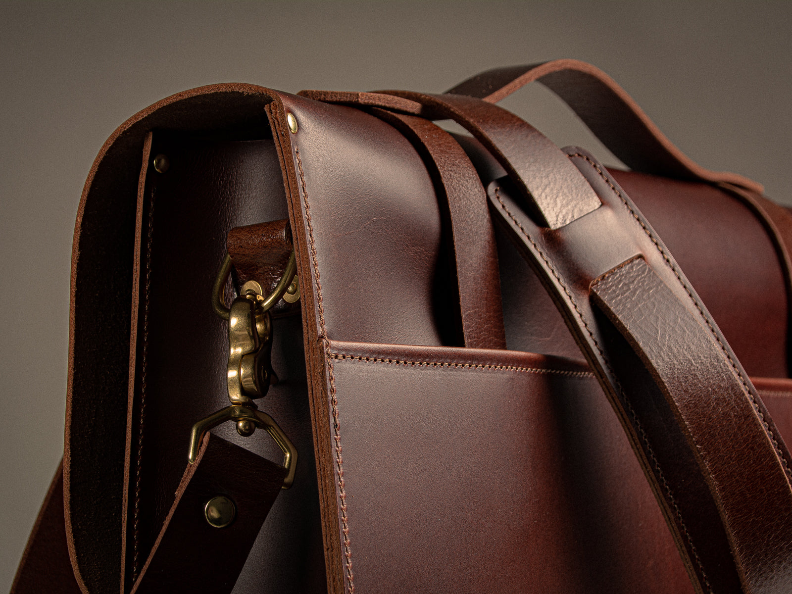 Close-up of a brown leather messenger bag, showing padded shoulder strap and solid brass hardware