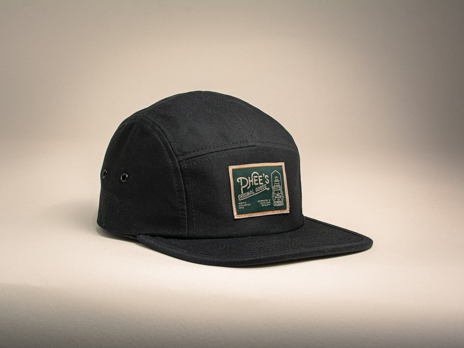 Black 5-panel hat with a woven label featuring an oil lamp sitting on a beige background
