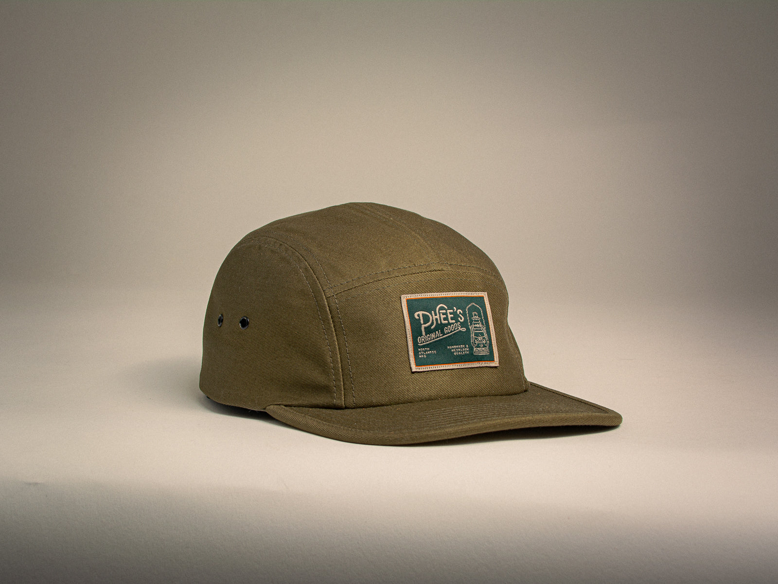 Olive 5-panel hat with a woven label featuring an oil lamp sitting on a beige background