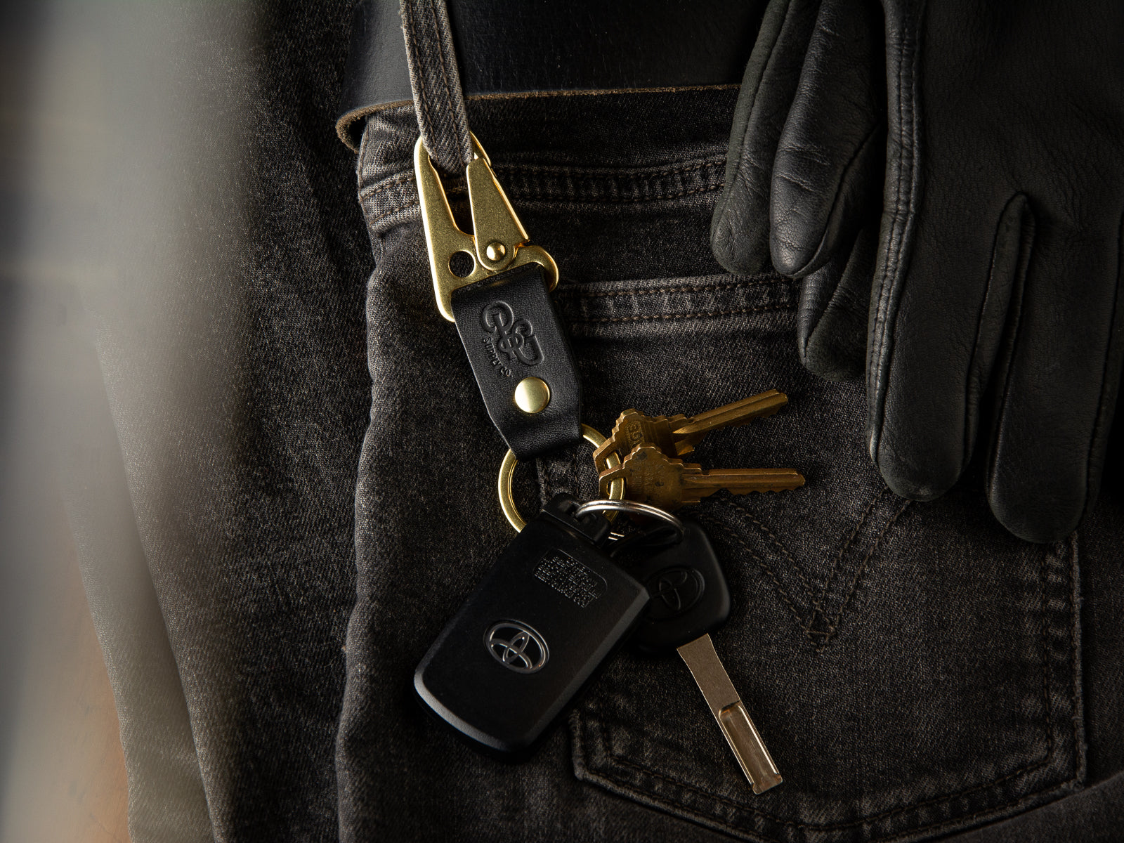 A black stubby keychain in full grain leather and brass hardware is clasped to a pair of LEvi's denims