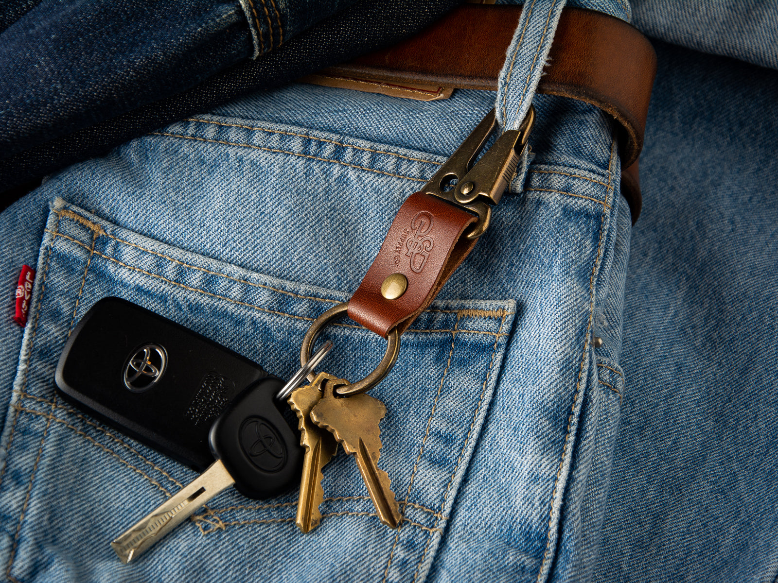 A brown stubby keychain in full grain leather and brass hardware is clasped to a pair of LEvi's denims