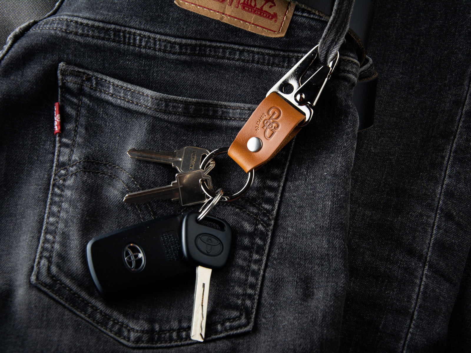 A tan stubby keychain in full grain leather and brass hardware is clasped to a pair of LEvi's denims