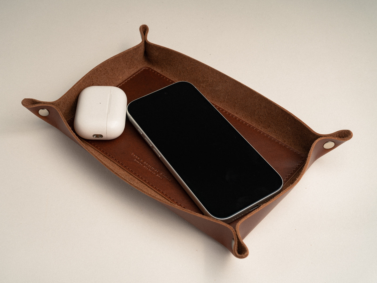 tan leather valet tray on a table with a phone and ear buds in it