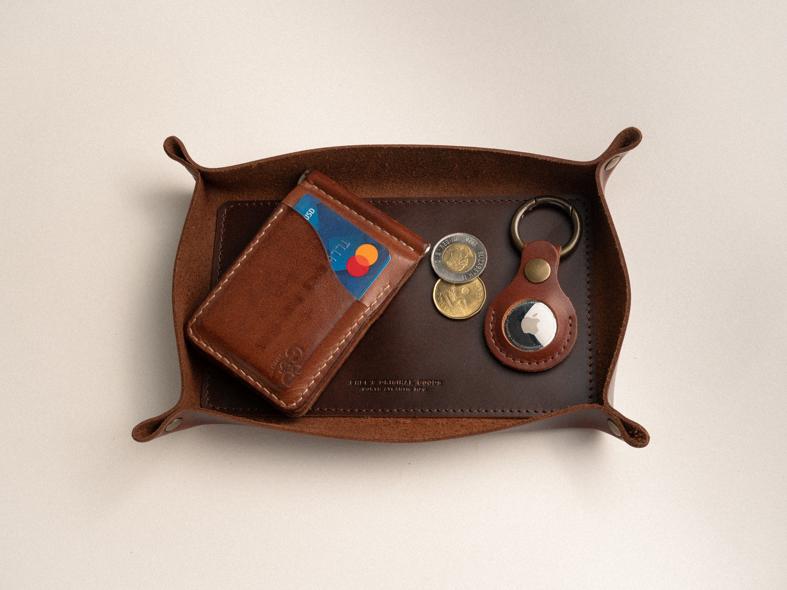 Brown leather valet tray on a table with wallet, money and airtag in it