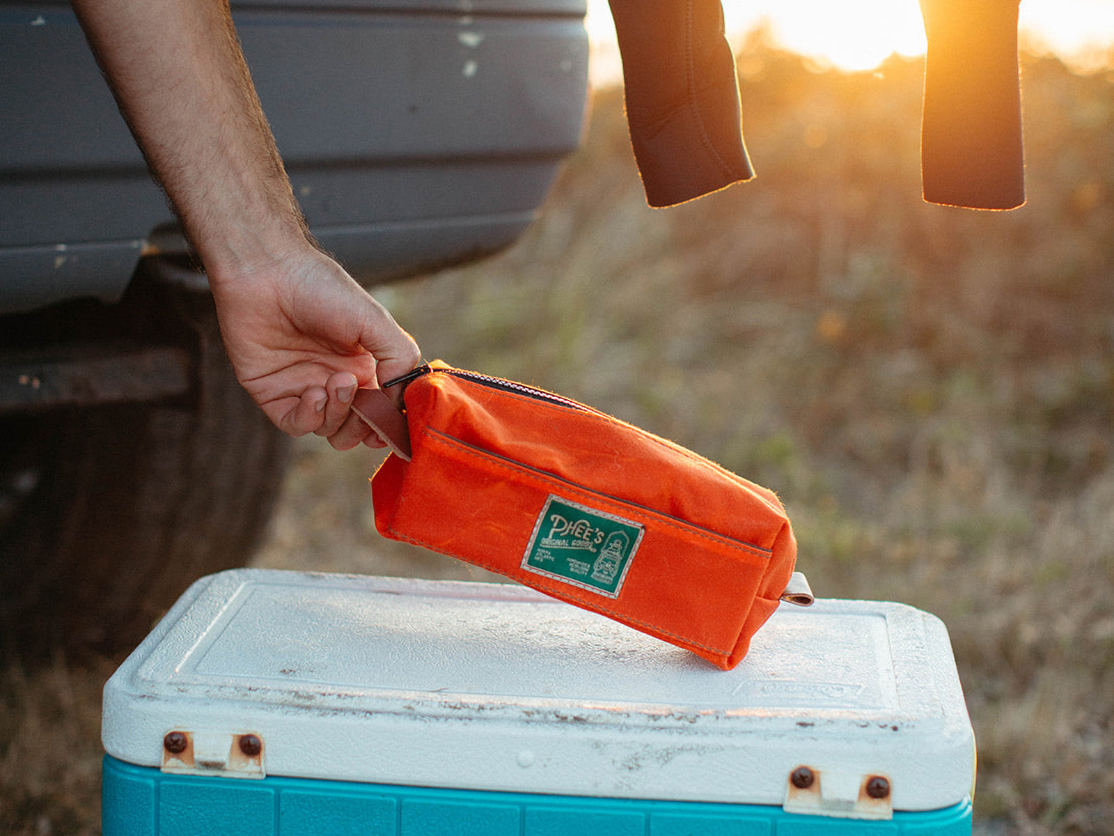 an orange waxed duck canvas washabuck shaving kit, being lifted off a cool box by the leather handle