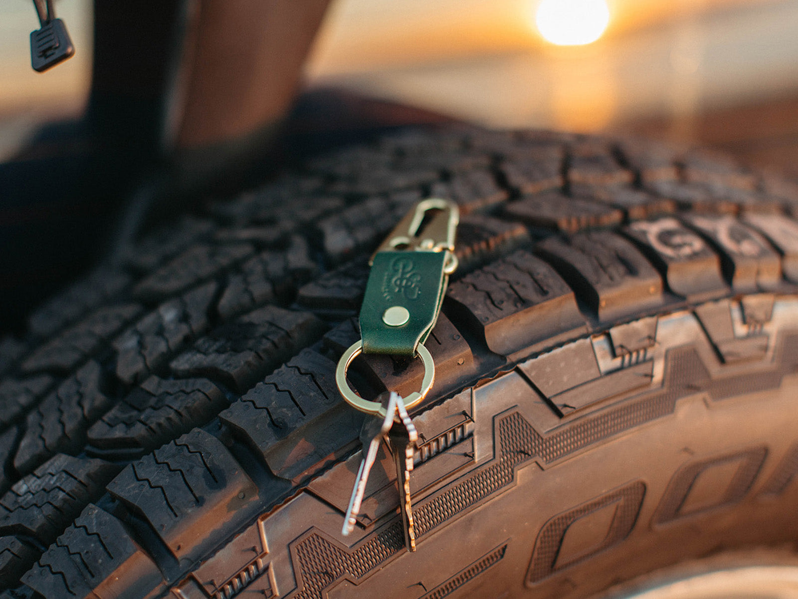 stubby leather keychain made with pine english bridle leather and solid brass hardware sitting on a tire