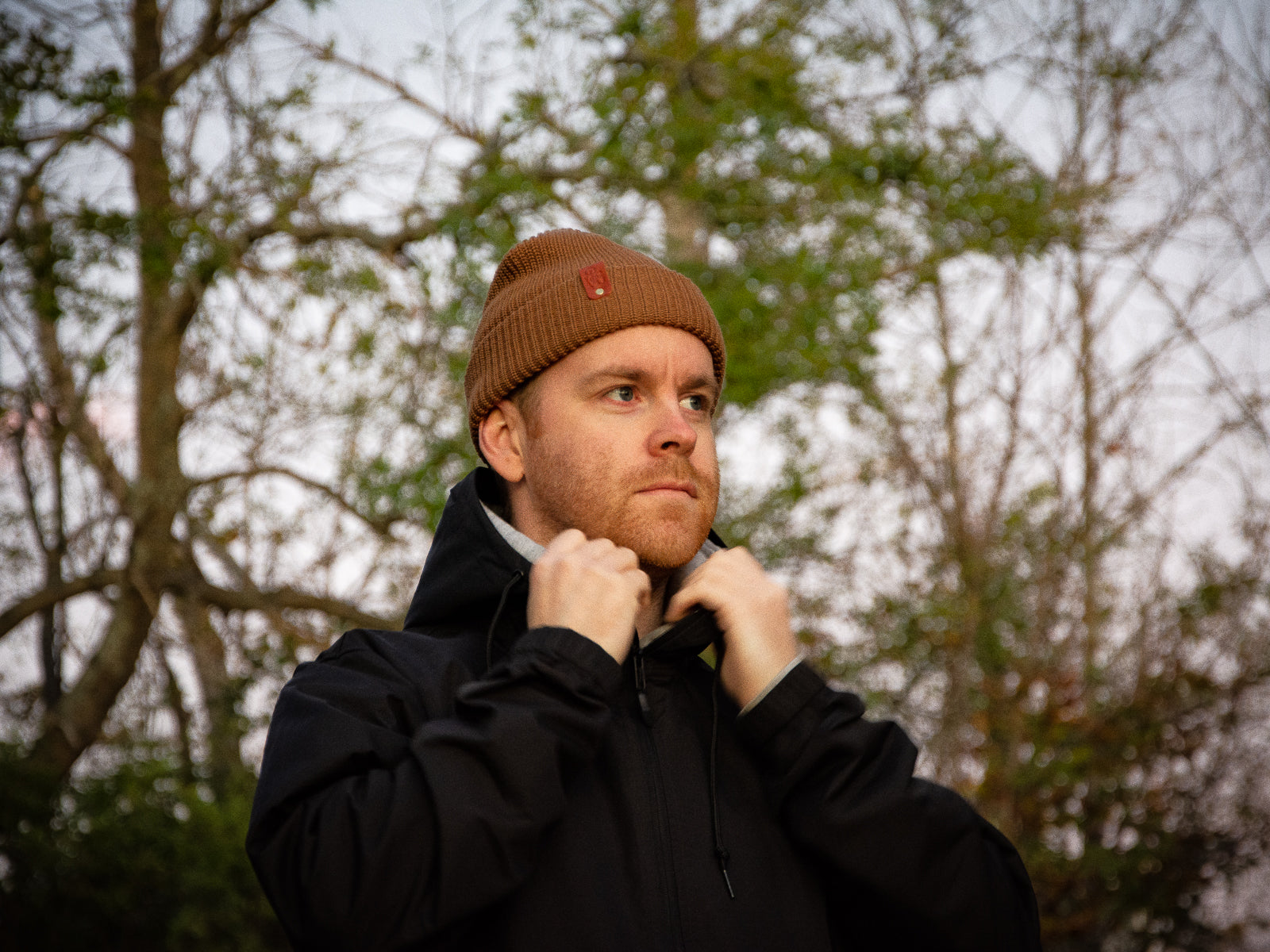 Kyle fixing his collar, weating a brown supply toque with a brown leather patch and brass rivet