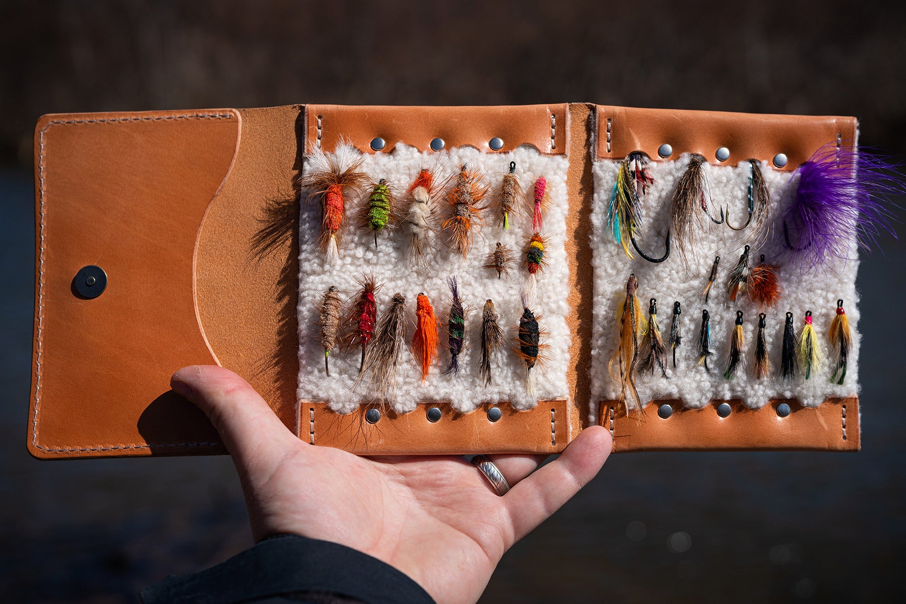 A fly fishing wallet full of colorfoul ties being held in hand.