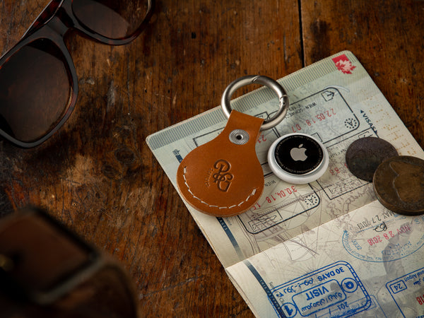 Veg-tan leather tan air tag holder keychain sitting on a passport