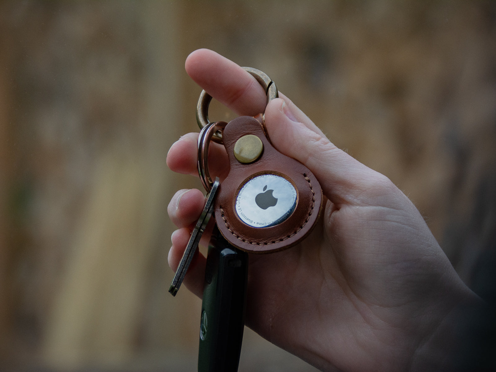 Hand holding a set of keys with brown leather air tag fob