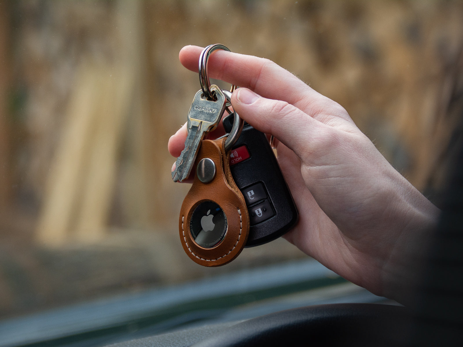 Hand holding car keys with a handmade leather air tag key fob in tan colour