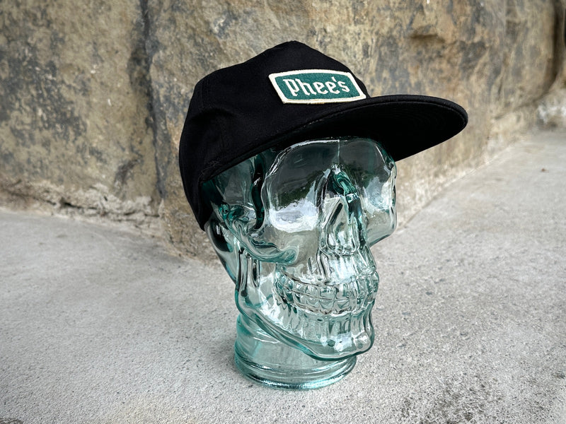 Black Phee's Badge Hat with embroidered green felt patch on a glass skull
