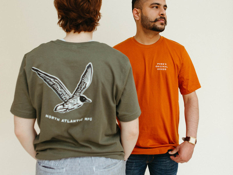 Shubham in the orange Gull Tee, Mads with their back to us, wearing the Olive Gull tee showing screenprinted back design