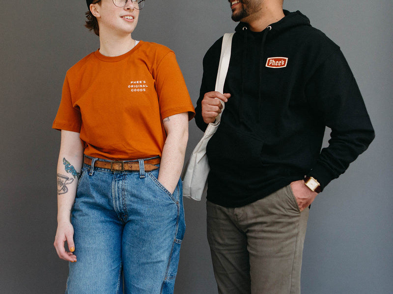 Two people chatting, one wearing a midweight Phee's Badge Hoodie in Black