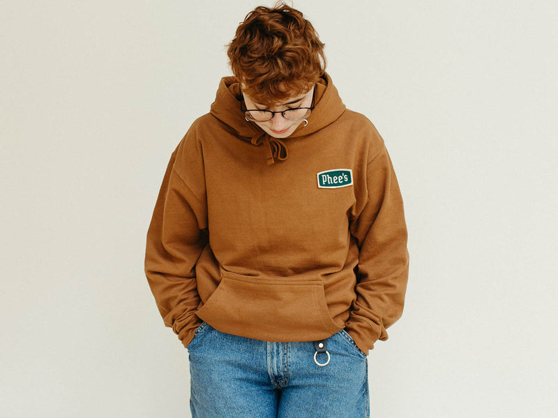 Mads with their hands in their pockets, cozied up in the saddle Phee's Badge hooded sweatshirt