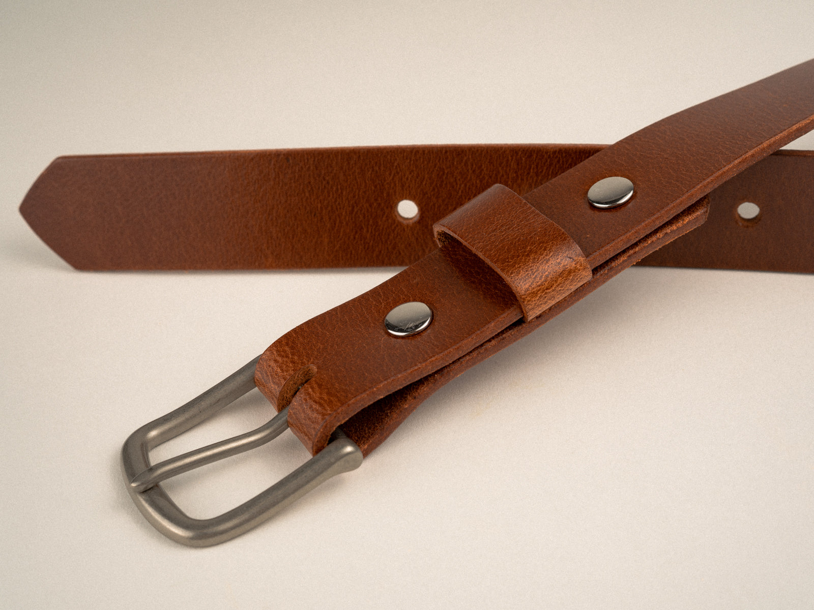 close up of tan leather ashfield belt with nickel hardware laying on a table