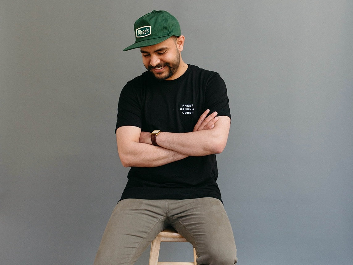 Shubham wearing a pine badge hat sitting on stool looking down