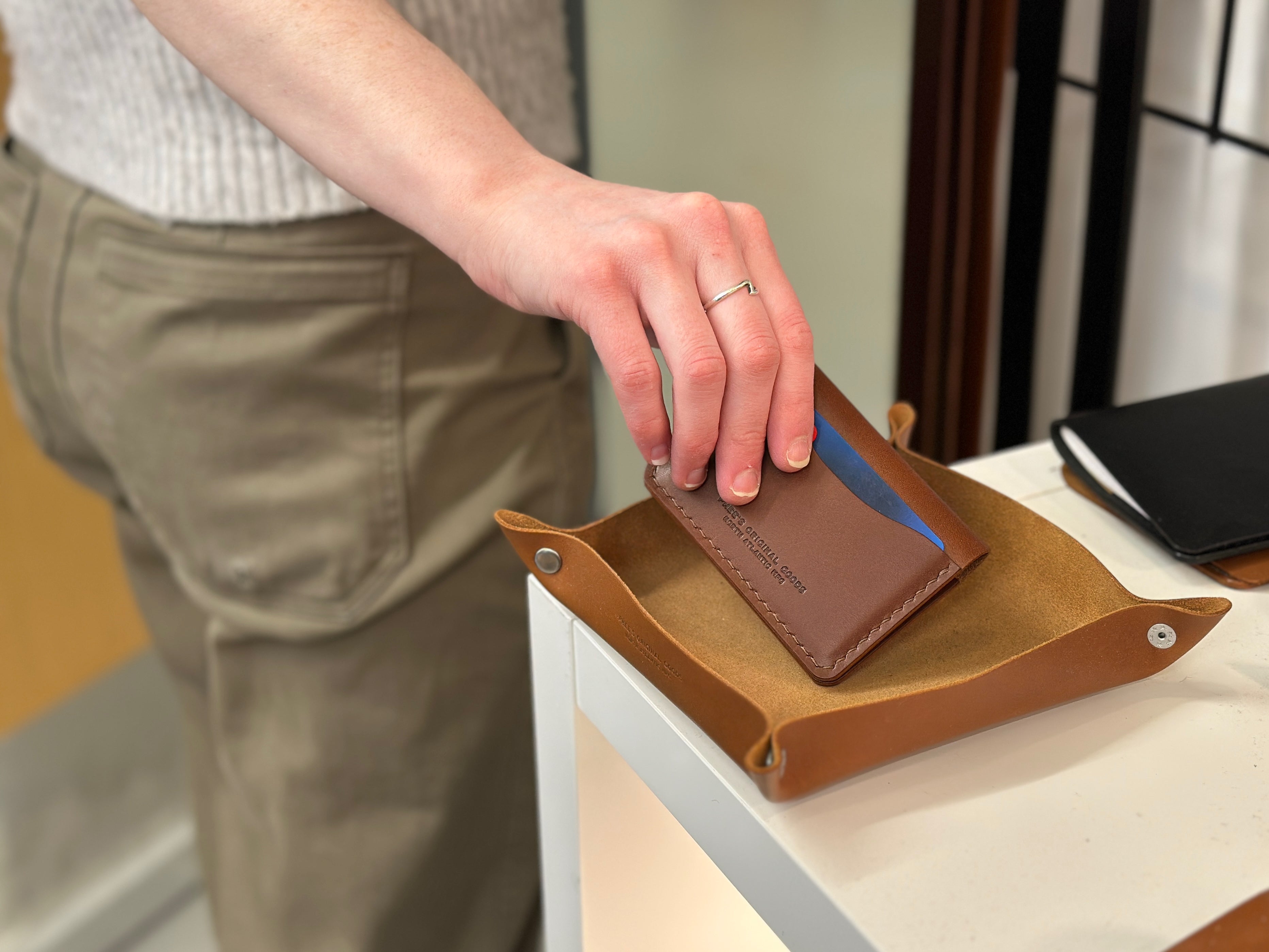 Someone picking up the brown belfry wallet from a leather valet tray