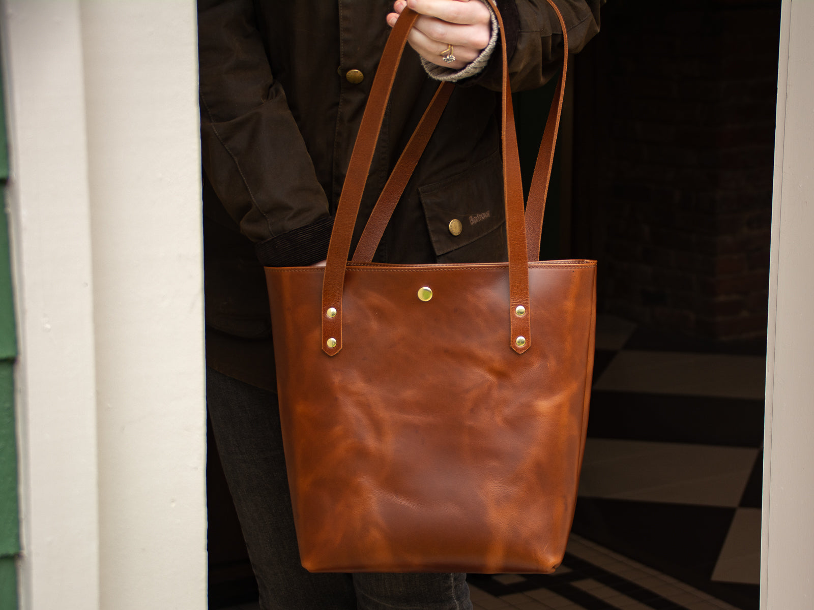 Big Bras d'Or Leather Tote Bag shown in door way with woman reaching into the depth of the bag.