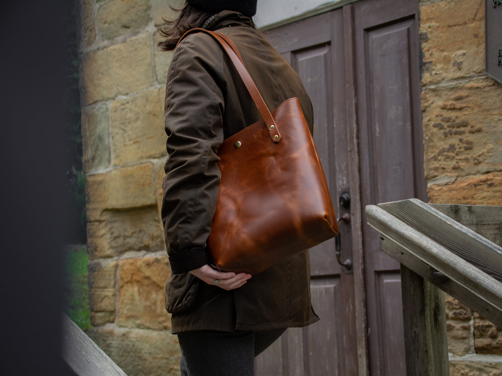 Big Bras d'Or Leather Tote Bag in Tan shown worn on woman's shoulder walking up stairs of heritage building.