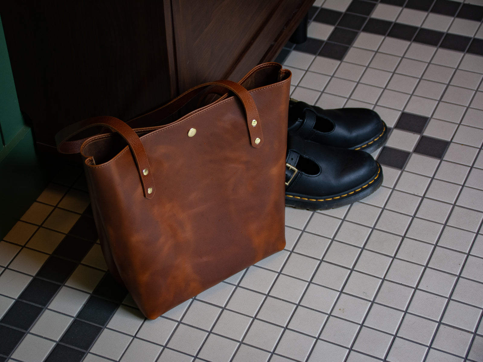 Big Bras d'Or Leather Tote Bag in tan shown next to Doc Martin shoes on porch floor.